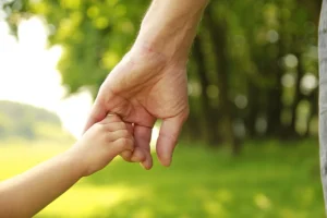 child and parent holding hands in green field
